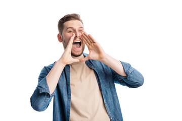 Handsome young guy in denim shirt screaming out loud while holding hands near open mouth. Satisfied...