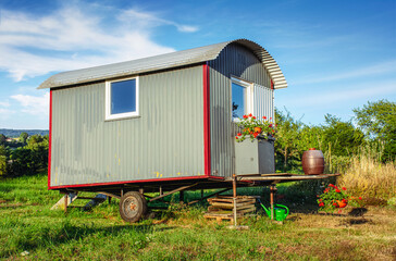 Fototapeta na wymiar Old building trailer as tiny house with flowers in rural landscape 