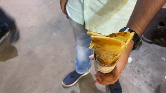 A man holds a Katti roll, a traditional Bengali street snack in which a paratha is packed with an egg, sometimes veggies, chicken or mutton kabab, and some sauces.