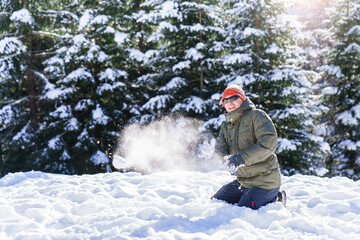 Fototapeta na wymiar Snowball fight. Young man playing in snow in winter and having fun in snowy forest. Family outdoors activities on Christmas holidays. Authentic lifestyle moment