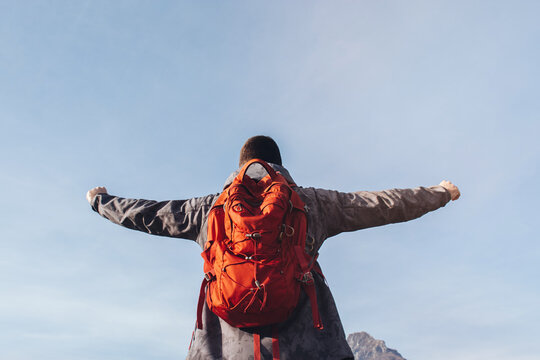 Soft Selective focus Rear view Man-traveler enjoying freedom with raised hands in the sky. A man with a tourist red backpack. Concept of tourist lifestyle, summer vacation outdoors.