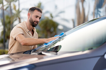 Man cleaning his car using micro fiber cloth. Car washing service concept 