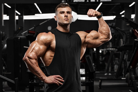 Muscular man in gym showing biceps muscles. Strong male