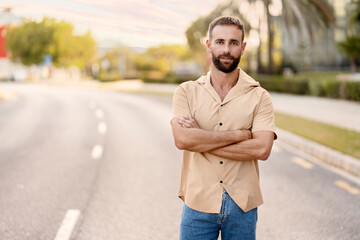 Portrait of handsome bearded latin man with arms crossed looking at camera standing on the road,...