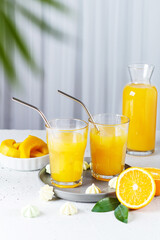 Glasses with orange juice, orange slices and mango on a gray background.