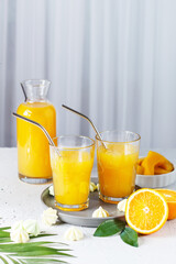 Glasses with orange juice, orange slices and mango on a gray background.