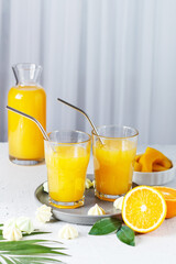 Glasses with orange juice, orange slices and mango on a gray background.