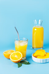 A glass with orange juice, orange and mango slices on a blue background.