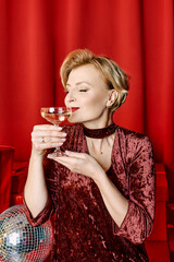 mature stylish elegant woman with glass of sparkling wine with presents on red background. Party, fashion, celebration, anti age concept 