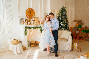 an attractive couple in blue clothes in room with fireplace and Christmas tree.