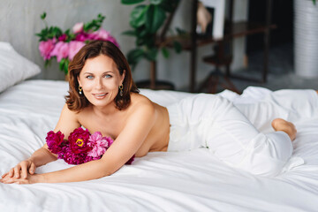Obraz na płótnie Canvas attractive brunette topless woman with a bouquet of peonies on the bed.