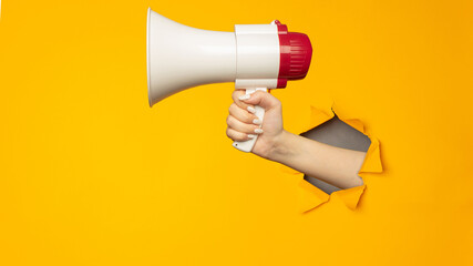 Woman holding megaphone in paper torn hole in yellow background with copy space.