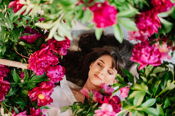 Naklejka premium a beautiful and gentle young woman lies in peony flowers. feminine beauty. 
