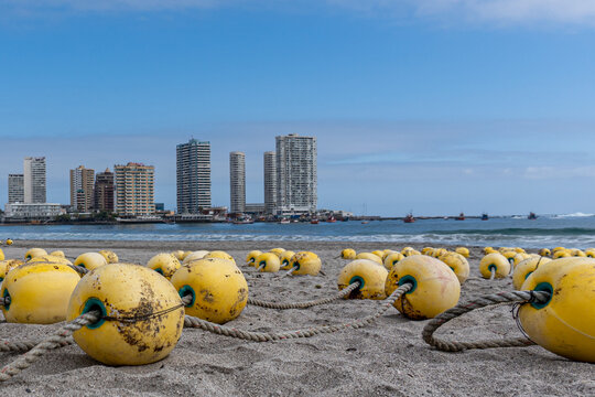 Ciudad de Iquique vista desde la playa con boyas en el primer plano y edificios en altura de fondo con barcos pesqueros 