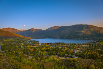 Beautiful view of mountain lake and town by the lake on nice fall evening in Colorado, USA. Blue sky, mountain range and rising moon in background