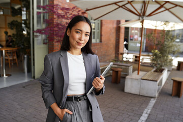 Young elegant professional leader Asian woman, female executive retail manager supervisor, small business owner wearing suit holding digital tablet standing outdoor looking at camera, portrait. - Powered by Adobe