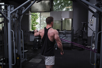 Rear view shot of a bodybuilder using resistance rubber band, working out at gym