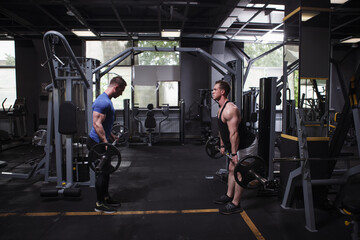Fototapeta na wymiar Twin brothers sportsmen facing each other at gym, doing barbell deadlift workout