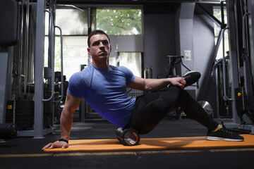 Fototapeta na wymiar Male athlete relaxing muscles after working out, using foam roller at gym