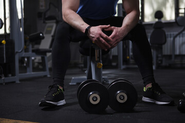 Unrecognizable sportsman resting at the gym, dumbbells lying near on the floor