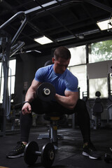 Fototapeta na wymiar Vertical shot of an athletic man doing dumbbells biceps curls exercise at gym