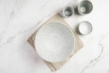 Empty grey ceramic scandy soup bowl, espresso coffee mugs and dip bowl, fork and knife on a marble surface and kitchen towel, top view