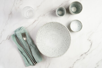 Empty grey ceramic scandy soup bowl, espresso coffee mugs and dip bowl, fork and knife on a marble surface and kitchen towel, top view