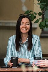 Portrait of smiling woman sitting in park cafe with cup of tea or coffee.