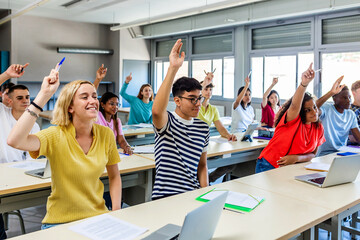 High school multiracial students group raising hand for teacher to ask a question during lecture in...