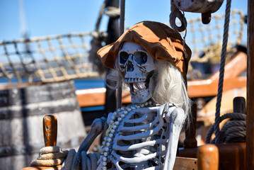 Spooky mock up pirate skeleton wearing a hat and a pearl necklace on a traditional sailing ship.