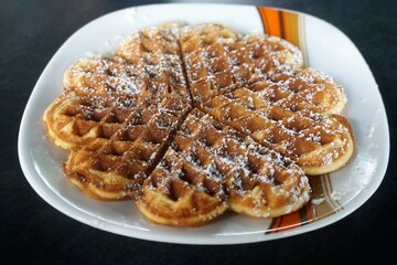 Frische Waffeln mit Puderzucker auf weißem Teller mit Muster
