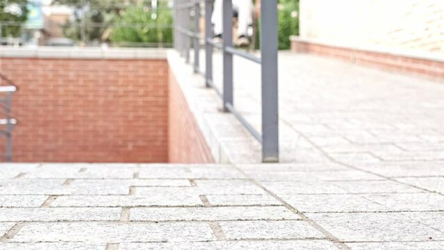 unrecognizable young man with dark skin in light clothes and black shoes in a wheelchair going down a ramp for disabled people with focused foreground and unfocused background