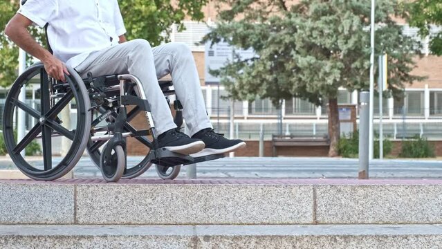 unrecognizable young man in a wheelchair approaches some steps and has to go because he cannot go down them
