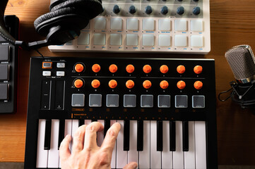 Close-up. Studio equipment. Modern midi keyboard and studio headphones, man's hand on the keys....