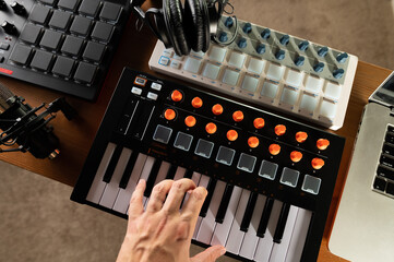 Man's hand on midi keyboard. Studio headphones. Low angle view. Modern equipment for recording studio, music studio. Workplace of a musician, composer, sound engineer.