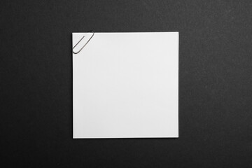Sheet of paper with clip on black background, top view