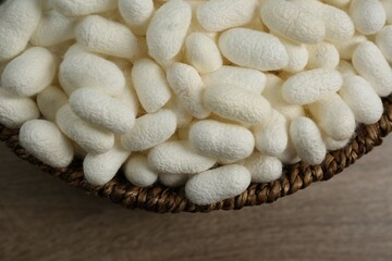 White silk cocoons in bowl on wooden table, closeup