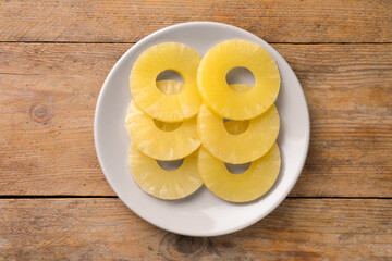 Plate with tasty canned pineapple rings on wooden table, top view