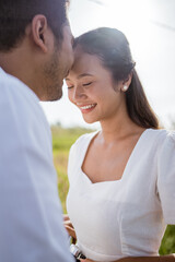 Fototapeta premium man kissing girlfriend on forehead in the street in the countryside. Romantic young man giving a kiss to his woman in the city street. Loving young couple