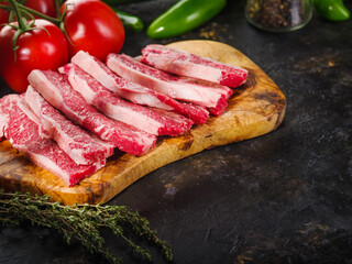 Homemade raw steaks on a cutting board, fresh vegetables, greens on a dark background. Recipes for home cooking. Healthy lifestyle. Banner, poster, advertising.