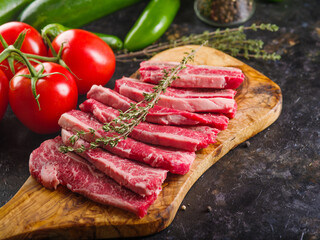 Homemade steaks on a wooden cutting board. Ready to cook. Fragrant sprig of rosemary, fresh tomatoes, peppers and spices. There are no people in the photo.