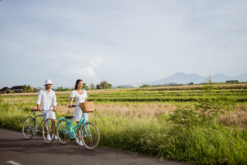 Obraz premium romantic couple push their bike as they are walking on the road in the countryside together