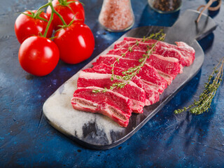 On a dark blue background, raw meat steaks, tomatoes, spices and seasonings in glass jars. Cooking meat steaks. Barbecue, grill, picnic, banquet.