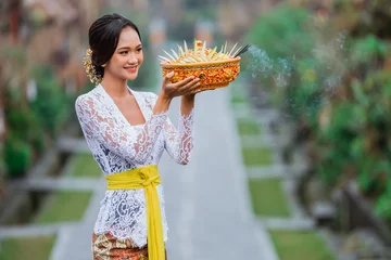 Fototapeten Bali beautiful balinese woman wearing traditional kebaya in the penglipuran bali village smiling while carrying offering for praying  © Odua Images