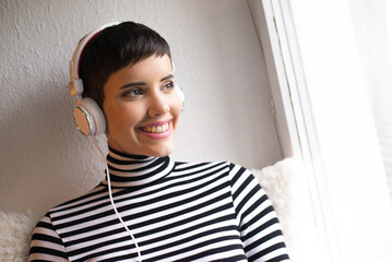 Young woman listening music on her headphones while sitting at home beside windows