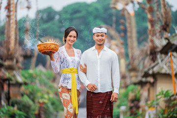 smiling balinese couple carrying an holy offering during galungan day in penglipuran village bali