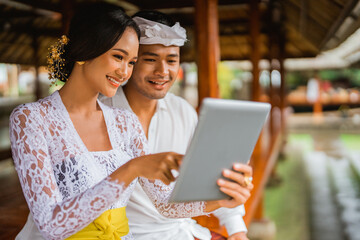 balinese man and woman with traditional clothes using tablet pc while sitting together