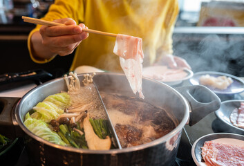 Woman boiling meat in hotpot. Hotpot is an interactive meal in which diners sit around a simmering...