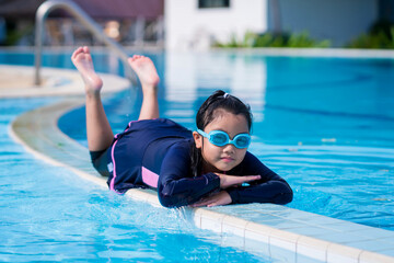 Naklejka premium little girl smiling wearing swimming glasses in swimming pool. children playing in swimming pool on summer.