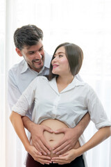 Young mother and her husband make heart symbol by hand on the pregnant wife stomach